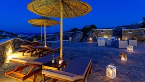 A beachside lounge area with wooden lounge chairs, thatched umbrellas, and stone walls. - Villa "Harmony' with Sea View, Private Pool & Wi-Fi (Mykonos)