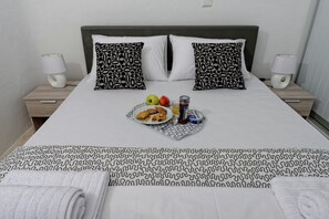 Una cama bien hecha con ropa de cama estampada, dos almohadas, lámparas de noche y una bandeja con comida y bebidas.