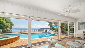 Ein Poolbereich mit Meerblick, Gartenmöbeln und einem Deckenventilator.