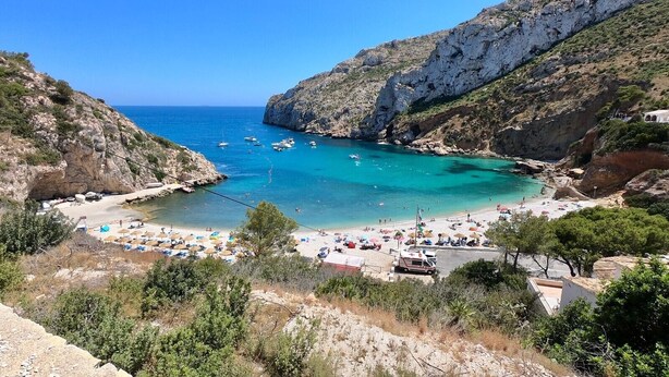 A coastal beach with rocky cliffs, clear turquoise waters, and beach umbrellas. - Casa de la Vista, Best Panoramic View on the Mediterranean (Benitachell)