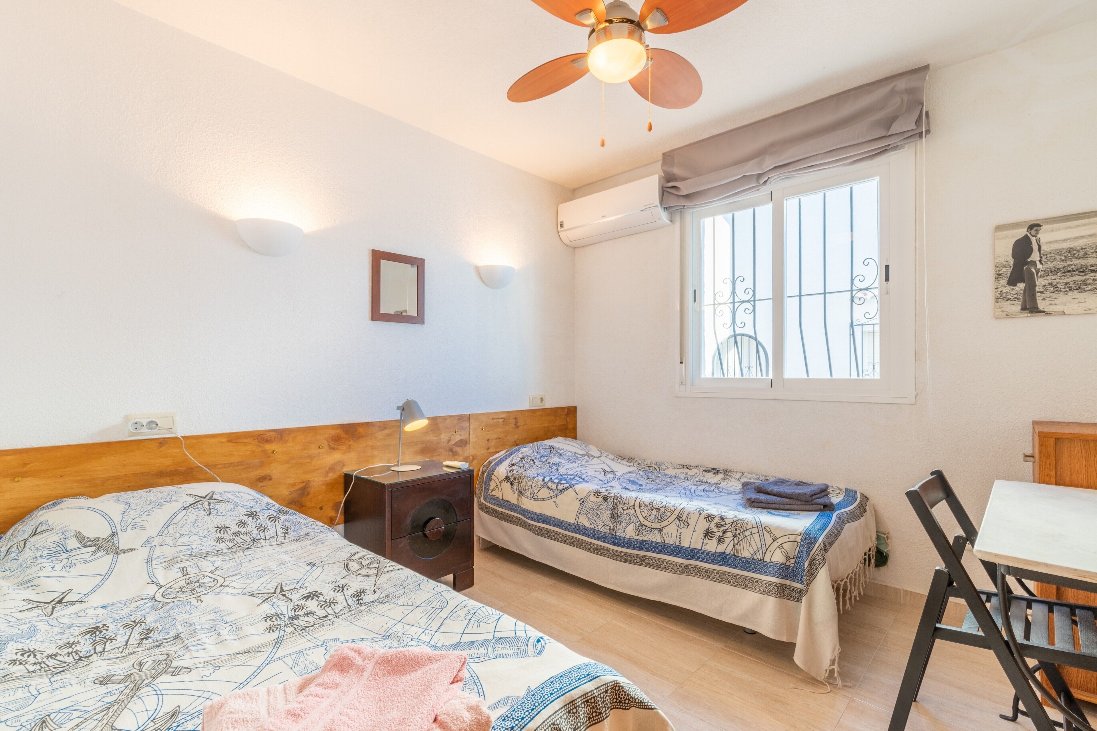 A bedroom with two beds, a ceiling fan, a table, and a window.