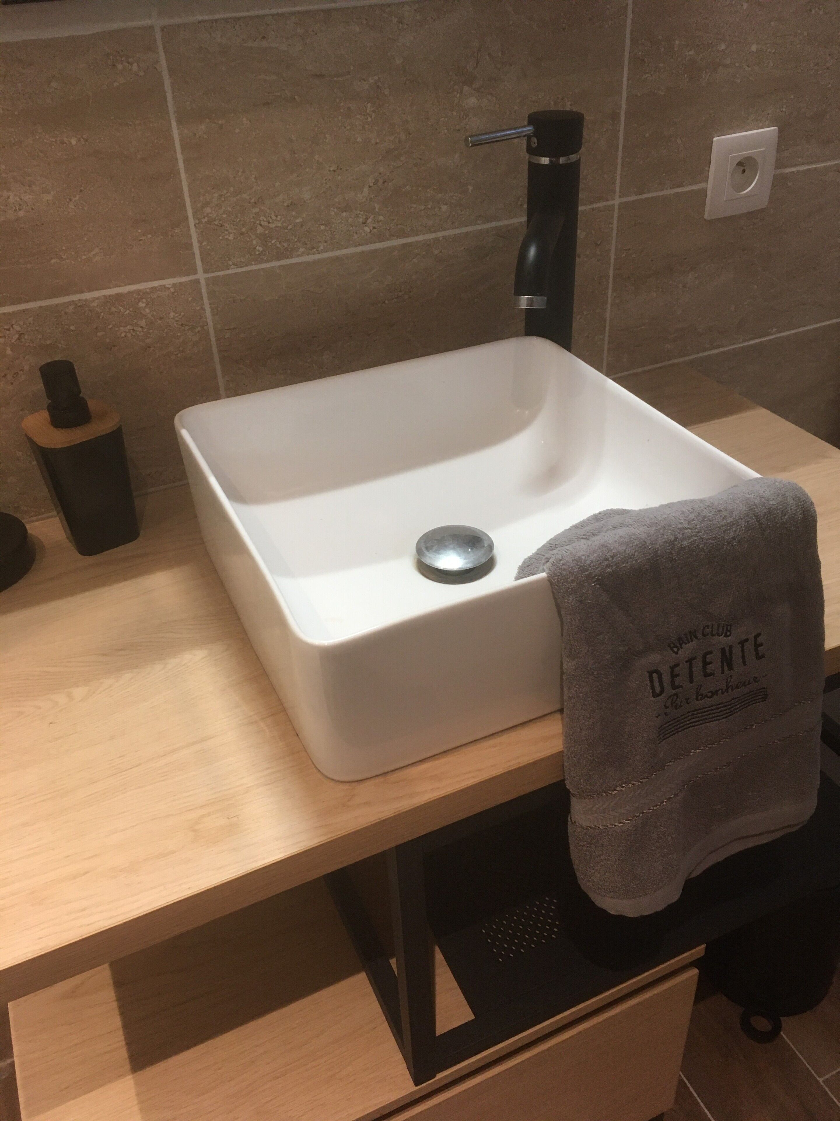 Un baño con un lavamanos blanco, un grifo negro y una toalla colgada a un lado.