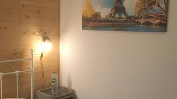 Une chambre à coucher avec un lit, une table de chevet, une lampe et un tableau représentant la Tour Eiffel.