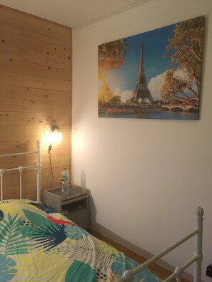 Ein Schlafzimmer mit einem Bett, einem Nachttisch, einer Lampe und einem Bild des Eiffelturms.