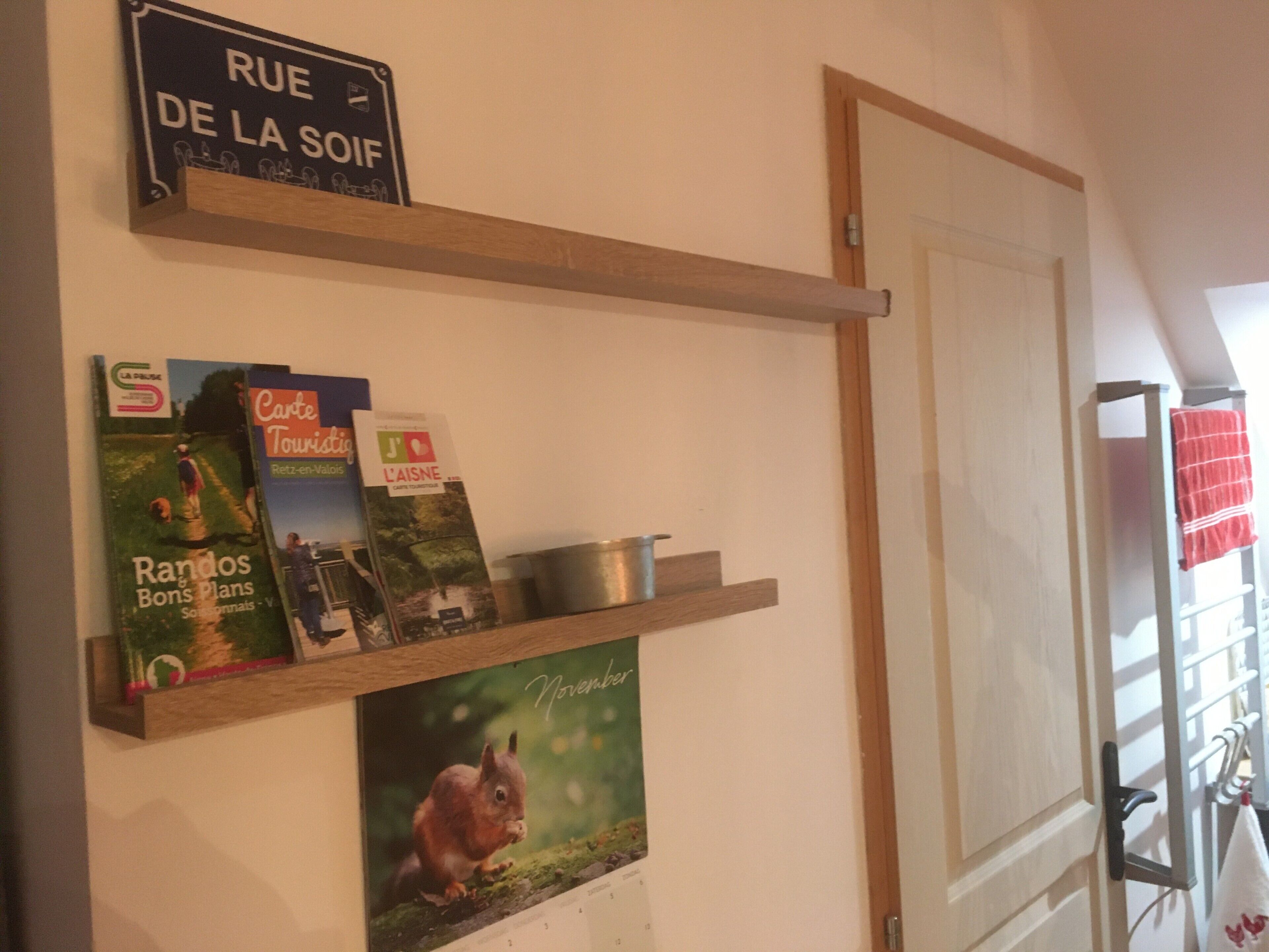 A wall with a calendar, a sign reading 'RUE DE LA SOIF,' and some books.