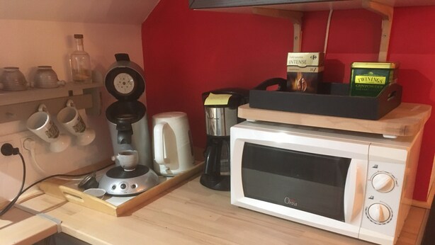 A kitchen counter with a coffee maker, a microwave, and a box of Twinings Gunpowder.