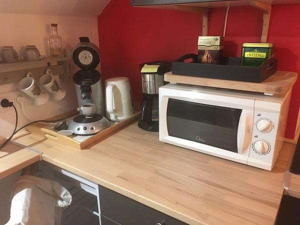 A kitchen counter with a coffee maker, a microwave, and a box of Twinings Gunpowder.