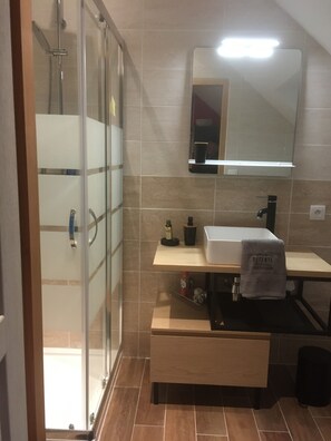 Ein modernes Badezimmer mit Duschkabine aus Glas, Waschbecken mit Handtuch und Spiegel über der Ablagefläche.