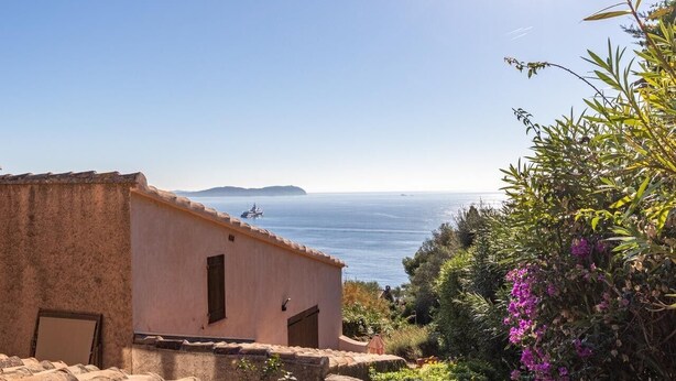 Un bâtiment situé sur la côte, offrant une vue sur la mer, avec un petit bateau et une végétation luxuriante.