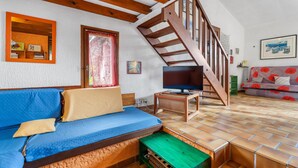 Un salon avec un escalier en bois, un canapé bleu, un téléviseur et un sol carrelé.