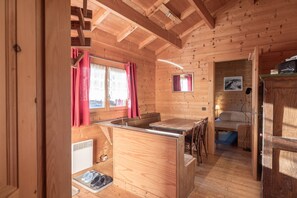 Ein Holzblockbau-Innenraum mit Essbereich, einem Bett und einem kleinen Fenster mit Vorhängen.