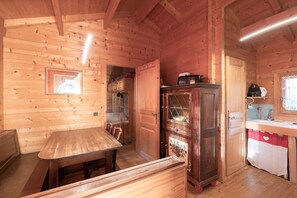 L’intérieur d’une cabane en bois comprend une table à manger, un banc, des armoires en bois et un coin cuisine avec un évier et un plan de travail.