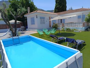 Ein Swimmingpool mit einer Leiter, umgeben von grünen Stühlen und einem weißen Gebäude mit einem gefliegelten Dach.
