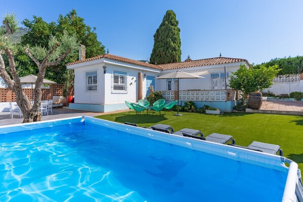 Um imóvel residencial com piscina, gramado e uma casa branca com telhado ladrilhado.
