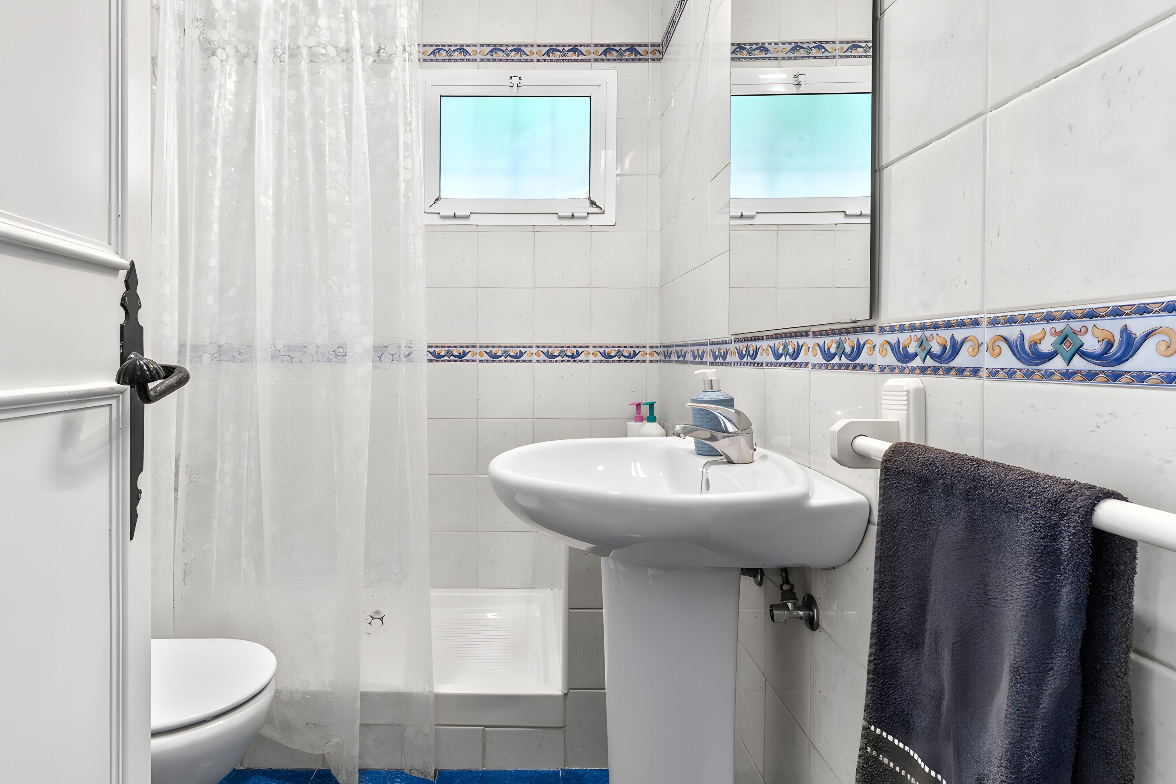 Une salle de bain avec un lavabo blanc, des toilettes, un rideau de douche et un porte-serviettes.