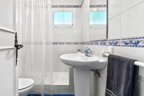 Um banheiro com pia branca, vaso sanitário, cortina de chuveiro e porta-toalhas.
