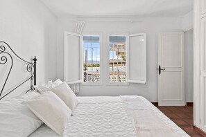 Quarto com cama, duas janelas, porta e vista para área externa.
