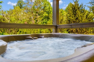 A hot tub with a wooden deck and metal railing, surrounded by lush greenery.