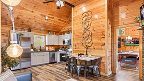 A cozy cabin interior with a dining area, kitchen, and a living room with a sofa and a dog. - Family Oasis By Ghosal Luxury Lodging (Sevierville)