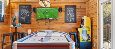 A cozy room with a pool table, a TV displaying a soccer game, and a pinball machine.