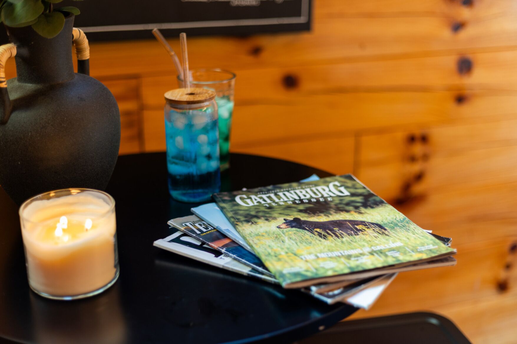 A table with a candle, a glass with a straw, a book titled 'Gatlinburg', and a vase with a plant.
