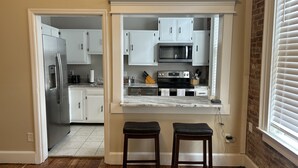 A kitchen with white cabinets, a stainless steel refrigerator, a microwave, and a stove. There are two wooden stools in front of the counter. - Historic Loft in Frankfort Entertainment District (Frankfort)