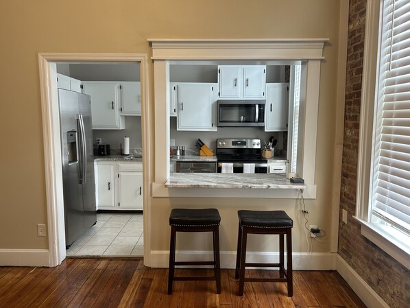 A kitchen with white cabinets, a stainless steel refrigerator, a microwave, and a stove. There are two wooden stools in front of the counter. - Historic Loft in Frankfort Entertainment District (Frankfort)