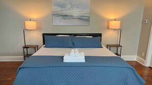 A neatly made bed with a blue quilt, two bedside lamps, and a painting of a seascape on the wall. - Historic Loft in Frankfort Entertainment District (Frankfort)