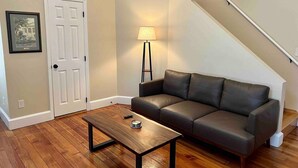 A living room with a wooden floor, a dark leather sofa, a wooden coffee table, a lamp, and a white door. - Historic Loft in Frankfort Entertainment District (Frankfort)