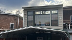 Ein zweistöckiges Haus mit überdachter Garage und einem großen Fenster im Obergeschoss.