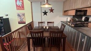 Ein Essbereich mit Holztisch und -stühlen, einer Hängelampe sowie eine Küche mit Holzausbau und einer Mikrowelle.