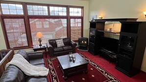 Ein Wohnzimmer mit Ledersofa, Couchtisch, Kamin und großen Fenstern mit Jalousien.