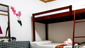 Quarto com duas beliches, um espelho e uma cama com almofada decorativa e flores.