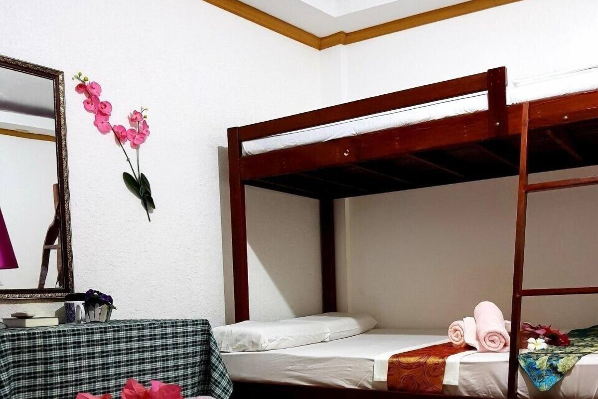 Una habitación con dos literas, un espejo y una cama con almohada decorativa y flores.