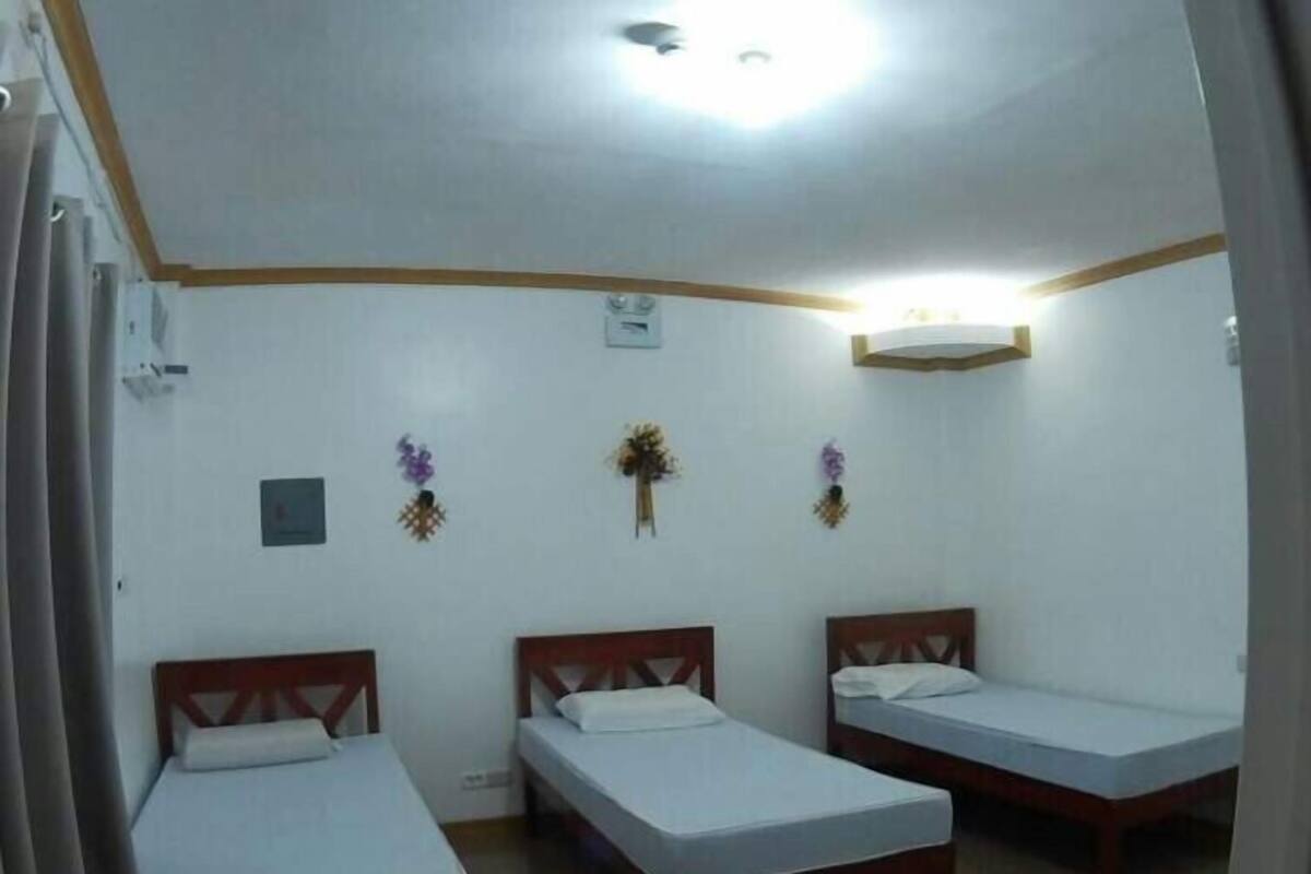 Una habitación con tres camas individuales, una lámpara en el techo y adornos en la pared.