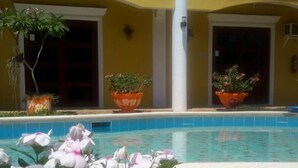 Uma área de piscina com piscina azul cristalina, cercada por vasos com plantas e flores.