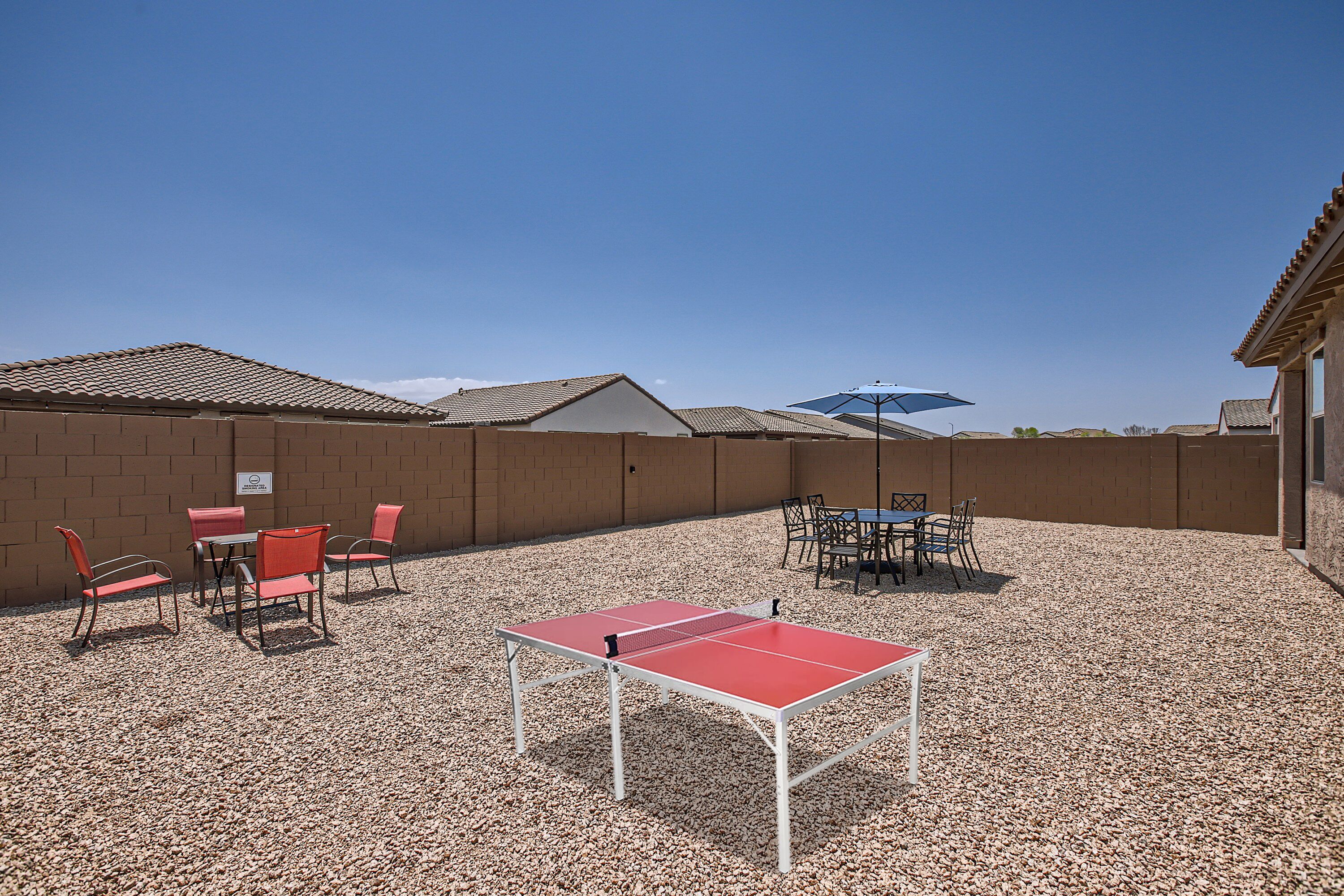 An outdoor area with a ping pong table, chairs, and an umbrella.