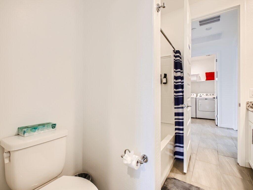 Egy fürdőszoba, amelyben található egy WC, egy törölközőtartó és egy zuhanyfüggöny.