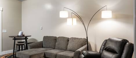 A living room with a sectional sofa, a black leather chair, and a small table with stools.