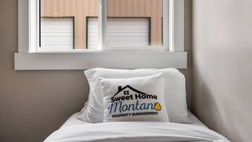 A bed with a pillow featuring a logo and text, a window with blinds, and a plain wall.