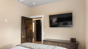 A bedroom with a bed, a dresser, a television on the wall, and a door leading to another room. - The Yellowstone Hideaway Unit C (West Yellowstone)