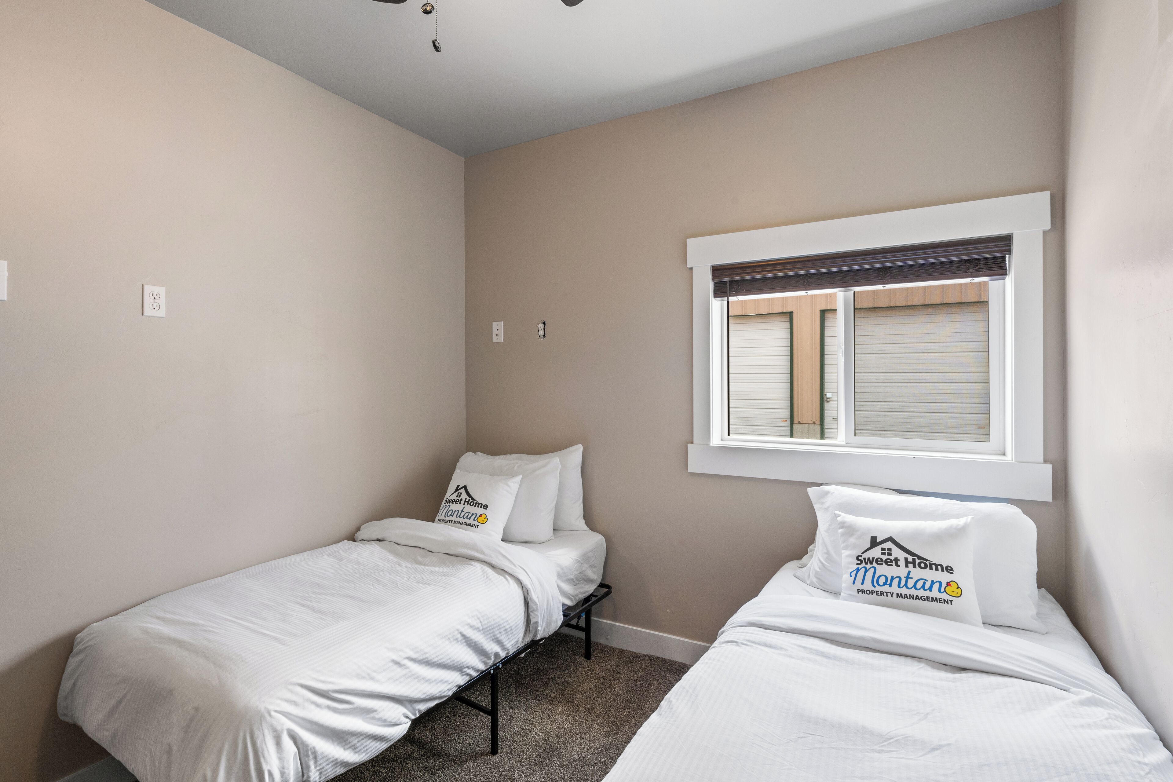 A bedroom with two single beds, a window with blinds, and a ceiling fan.