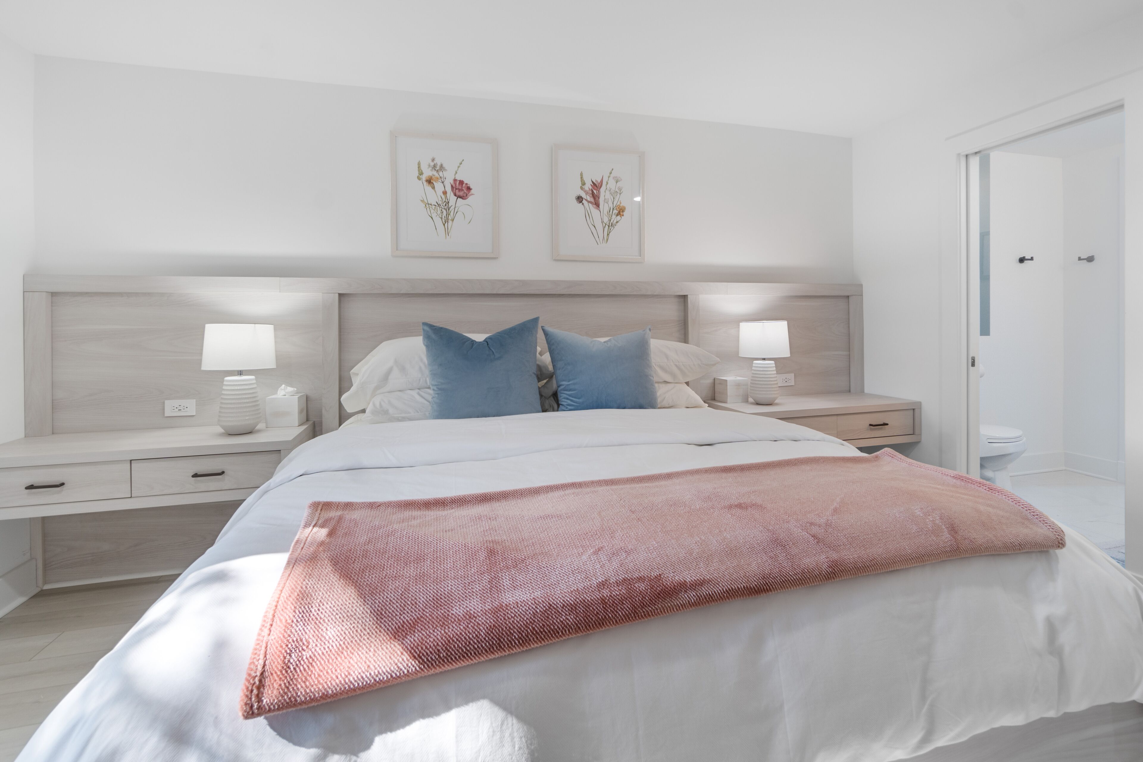 Une chambre à coucher moderne avec un grand lit, deux tables de chevet avec des lampes, une table de nuit et une étagère fixée au mur.