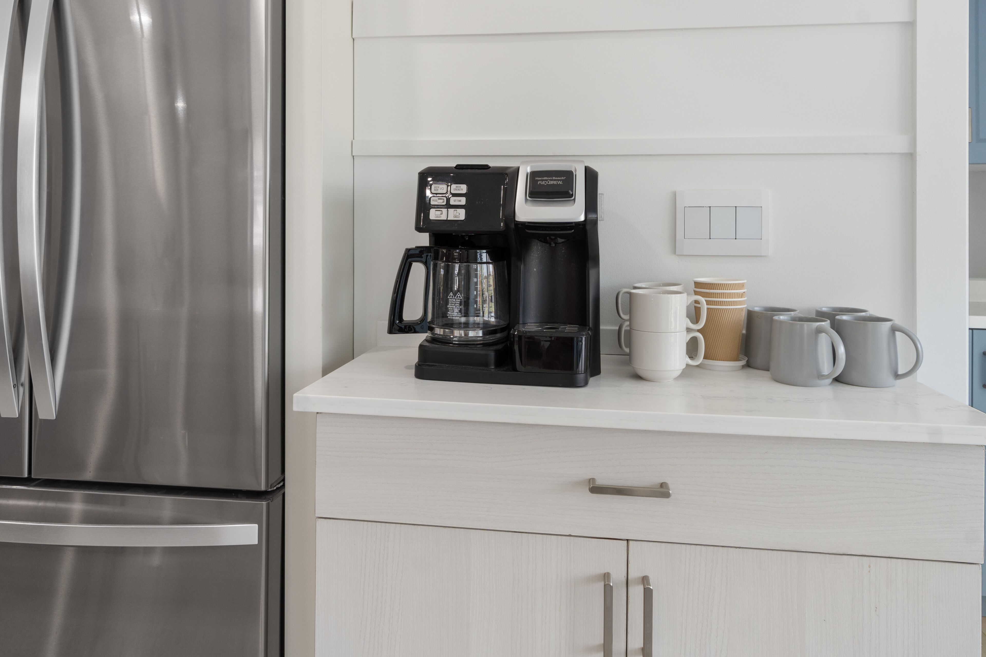 Una cucina con frigorifero in acciaio inossidabile, macchina del caffè nera e piano di lavoro bianco.