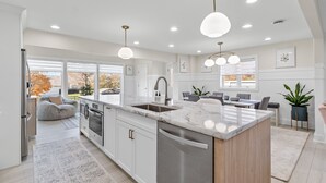 Une cuisine moderne dotée d’un grand îlot central, d’appareils électroménagers en acier inoxydable et de luminaires suspendus.