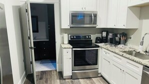 Una cocina con armarios blancos, microondas de acero inoxidable, estufa y cafetera.