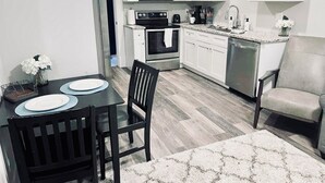 Una cocina moderna con armarios blancos, microondas, estufa y lavavajillas. Hay una mesa con platos y una silla.