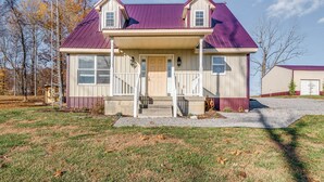 A two-story house with a front porch, a garage, and a metal roof. - Peaceful Russell Springs Home w/ Fire Pit & Pond! (Russell Springs)