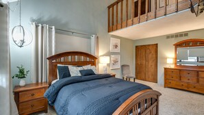 Quarto com cama de madeira, mesas de cabeceira, cômoda, cadeira e um mezanino com balaustrada de madeira.