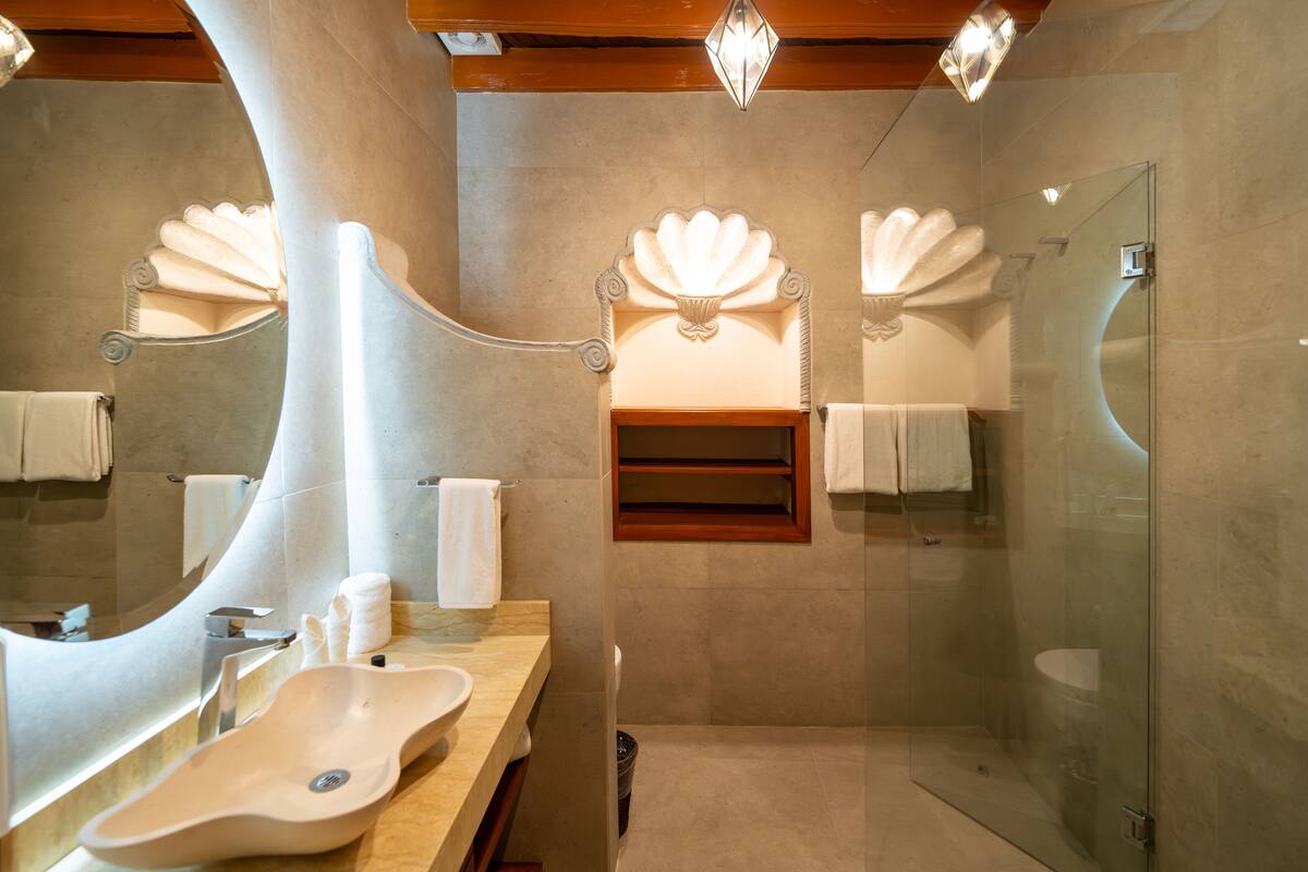 A modern bathroom with a large curved mirror, a beige sink, and a glass-enclosed shower.